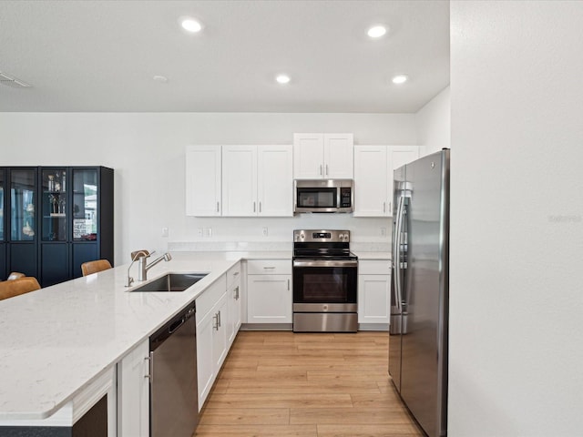 17729 Nectar Flume Dr, Land O Lakes, FL 34638 - kitchen with stainless steel appliances, a sink, a peninsula, white cabinetry, and light wood-style flooring