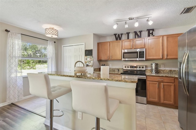 4528 Winding River Way, Land O Lakes, FL 34639 - kitchen featuring appliances with stainless steel finishes, a kitchen bar, light stone counters, a center island with sink, and brown cabinetry