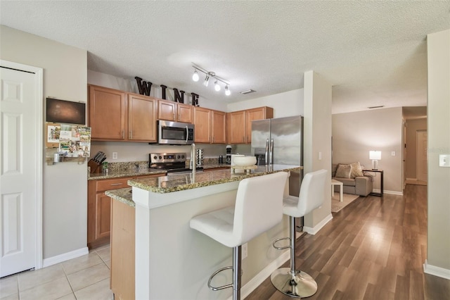 4528 Winding River Way, Land O Lakes, FL 34639 - kitchen featuring appliances with stainless steel finishes, stone counters, a breakfast bar area, a center island with sink, and a textured ceiling