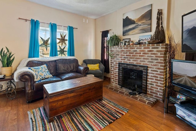 living room with wood finished floors, a textured ceiling, and a brick fireplace