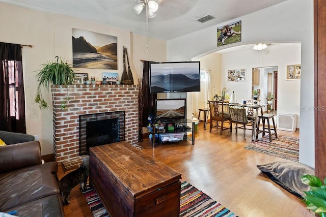 living area with ceiling fan, wood finished floors, a fireplace, arched walkways, and a textured ceiling
