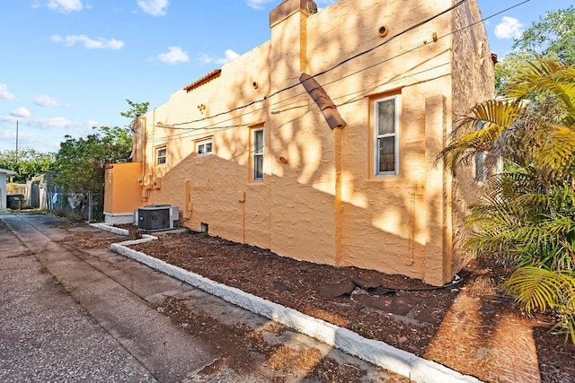 view of property exterior featuring central AC unit, fence, and stucco siding
