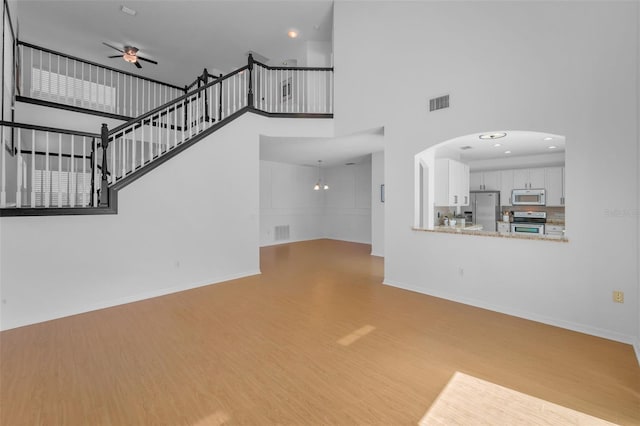 3002 Savannah Oaks Cir, Tarpon Springs, FL 34688 - unfurnished living room featuring ceiling fan, a towering ceiling, wood finished floors, stairway, and baseboards