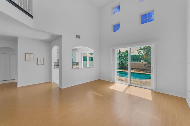 3002 Savannah Oaks Cir, Tarpon Springs, FL 34688 - unfurnished living room featuring wood finished floors, baseboards, a high ceiling, and arched walkways