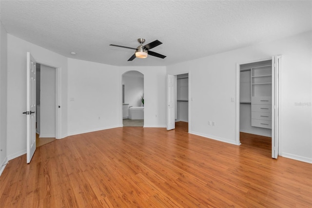 3002 Savannah Oaks Cir, Tarpon Springs, FL 34688 - unfurnished bedroom with light wood-style floors, a textured ceiling, arched walkways, connected bathroom, and baseboards