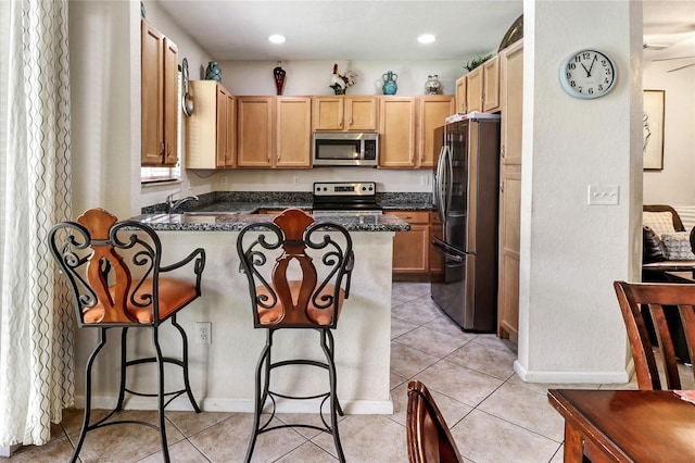 21115 NW 14th Pl Unit 2, Miami, FL 33169 - kitchen featuring stainless steel appliances, a peninsula, a kitchen breakfast bar, dark stone countertops, and light brown cabinets