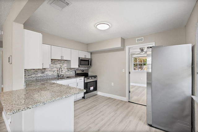 1310 43rd St S, Saint Petersburg, FL 33711 - kitchen featuring appliances with stainless steel finishes, light wood-style floors, white cabinetry, light stone countertops, and a peninsula