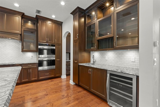 1171 Red Maple Cir NE, Saint Petersburg, FL 33703 - kitchen featuring wine cooler, double oven, arched walkways, light wood-style flooring, and tasteful backsplash