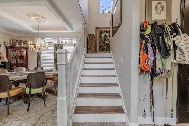 stairway with a chandelier, a raised ceiling, ornamental molding, and baseboards