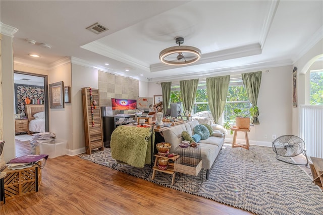 living room featuring a raised ceiling, baseboards, ornamental molding, wood finished floors, and arched walkways