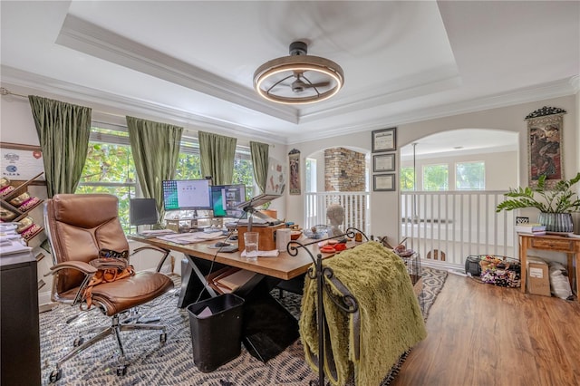 office area featuring a raised ceiling, ornamental molding, wood finished floors, and arched walkways