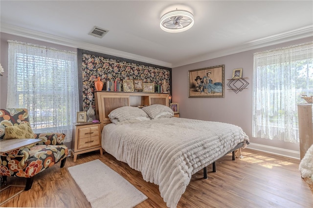 bedroom with ornamental molding, multiple windows, wood finished floors, and baseboards