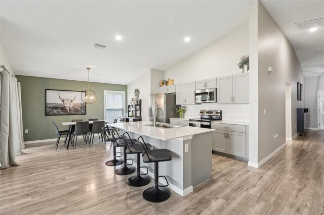 kitchen with stainless steel appliances, a sink, a breakfast bar area, a kitchen island with sink, and light wood-style floors