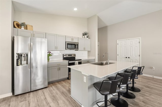 kitchen with appliances with stainless steel finishes, a sink, gray cabinets, backsplash, and a breakfast bar
