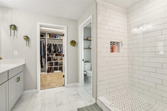 bathroom with marble look tiles, toilet, a tile shower, vanity, and a spacious closet