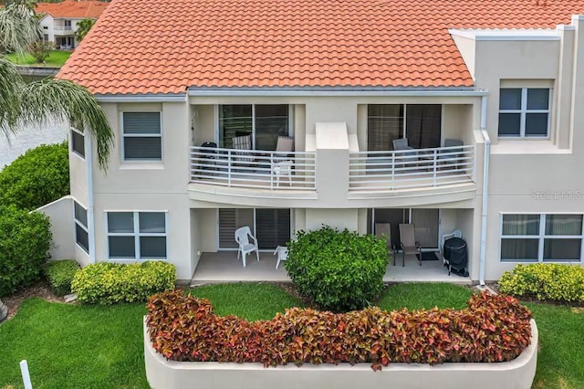 back of house with a balcony, stucco siding, a patio area, and a tile roof