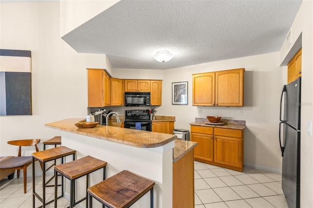kitchen featuring black appliances, a peninsula, light tile patterned flooring, a textured ceiling, and baseboards