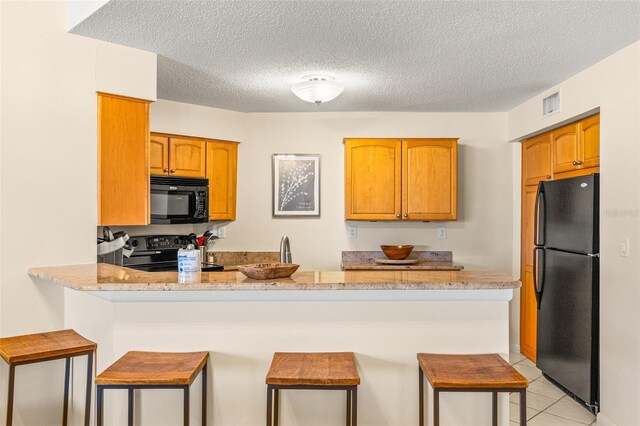 kitchen with black appliances, a peninsula, a breakfast bar, a textured ceiling, and light stone countertops
