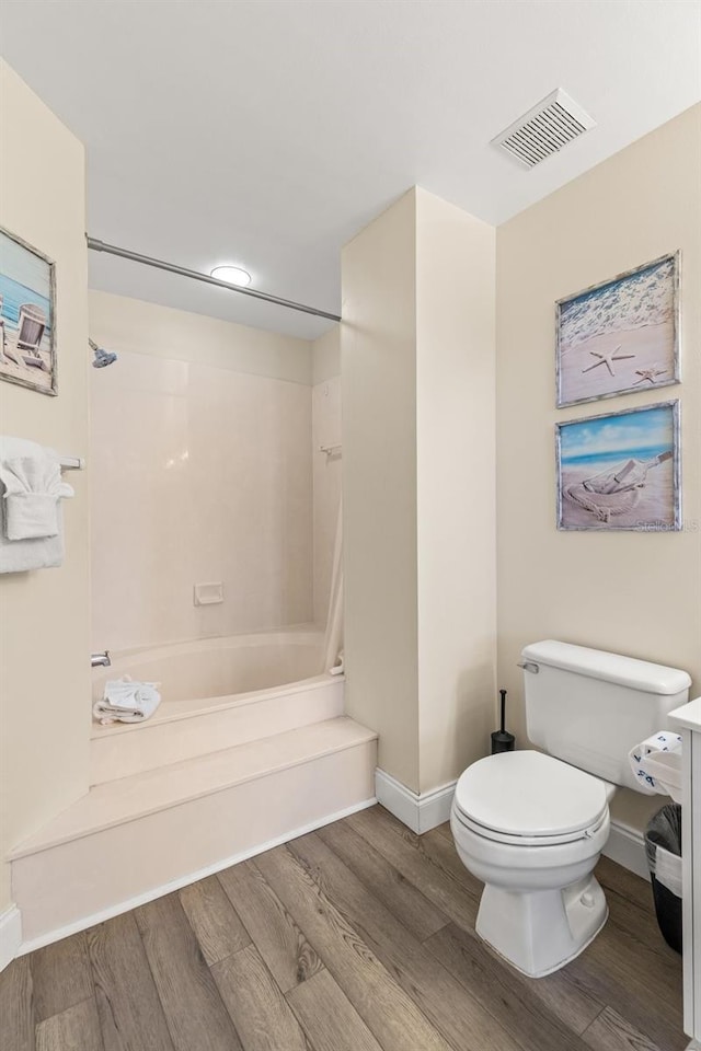 full bathroom with wood finished floors, toilet, baseboards, and shower / washtub combination