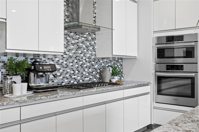 199 Dali Blvd Unit 2, Saint Petersburg, FL 33701 - kitchen featuring wall chimney exhaust hood, stainless steel appliances, white cabinetry, light stone countertops, and tasteful backsplash
