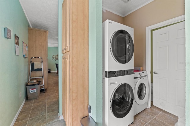 laundry area with stacked washer / dryer, tile patterned floors, a textured ceiling, baseboards, and crown molding