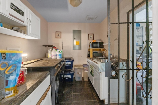 kitchen with electric panel, white cabinetry, black microwave, a sink, and dark tile patterned floors