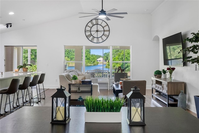 dining room with a ceiling fan, high vaulted ceiling, arched walkways, wood finished floors, and baseboards