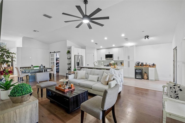 living room with a barn door, a ceiling fan, wine cooler, wood finished floors, and recessed lighting