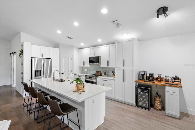 kitchen with appliances with stainless steel finishes, wine cooler, a kitchen bar, a sink, and tasteful backsplash