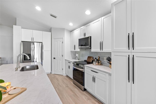 kitchen with stainless steel appliances, a sink, tasteful backsplash, light stone counters, and white cabinetry