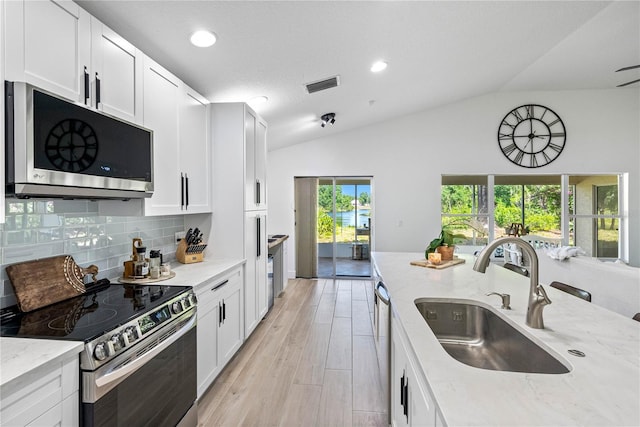 kitchen with stainless steel appliances, a sink, vaulted ceiling, light stone counters, and tasteful backsplash