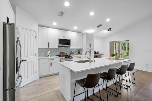 kitchen with appliances with stainless steel finishes, a sink, a kitchen bar, tasteful backsplash, and light wood-type flooring