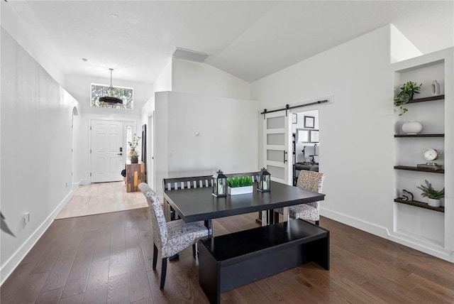 dining area with a barn door, dark wood finished floors, healthy amount of natural light, baseboards, and high vaulted ceiling