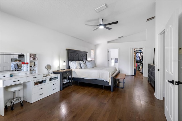 bedroom featuring lofted ceiling, a walk in closet, dark wood-type flooring, a closet, and a ceiling fan