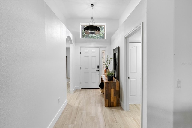 entryway with light wood-style flooring, arched walkways, baseboards, a chandelier, and a towering ceiling