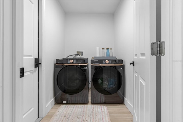clothes washing area with washing machine and dryer, light wood-style floors, and baseboards