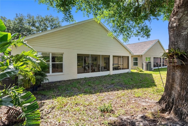 rear view of house featuring central AC, a sunroom, stucco siding, and a lawn