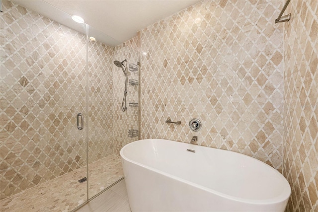 31645 Bugle Ln, Wesley Chapel, FL 33543 - bathroom featuring a freestanding tub, a stall shower, tile patterned flooring, and tile walls