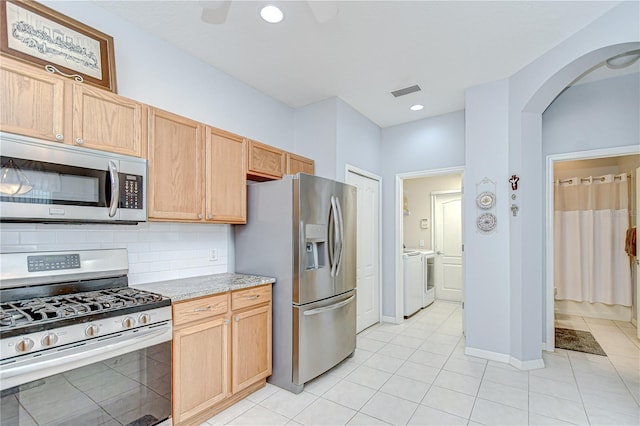 6030 Sandhill Ridge Dr, Lithia, FL 33547 - kitchen with stainless steel appliances, washing machine and dryer, arched walkways, light tile patterned floors, and decorative backsplash