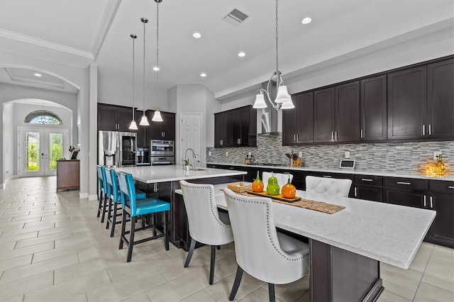 kitchen with a large island, ornamental molding, arched walkways, french doors, and appliances with stainless steel finishes