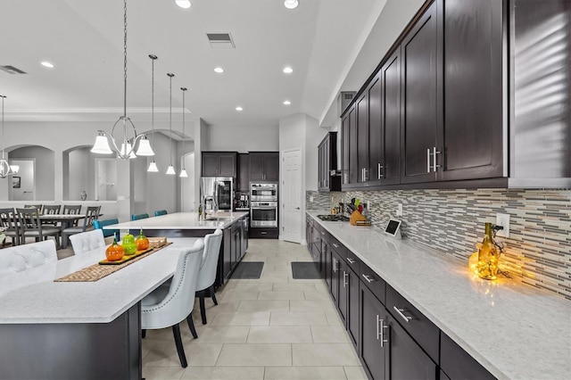 kitchen with a chandelier, appliances with stainless steel finishes, a kitchen bar, backsplash, and recessed lighting