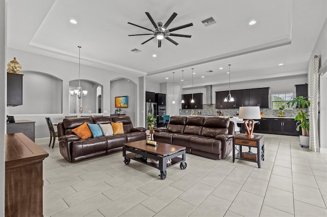 living room with a tray ceiling, arched walkways, a chandelier, ceiling fan, and recessed lighting