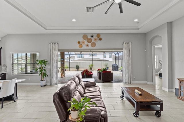 living room featuring arched walkways, a tray ceiling, ceiling fan, light tile patterned flooring, and baseboards