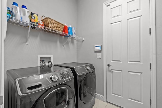 washroom featuring washing machine and dryer, light tile patterned flooring, and baseboards