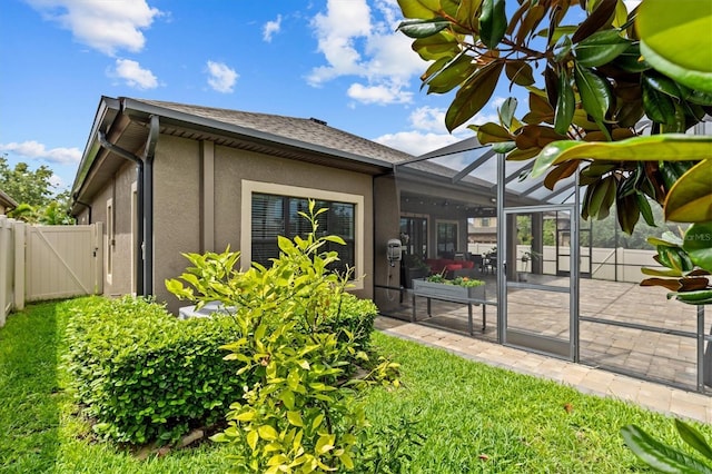 view of home's exterior with a patio, a gate, stucco siding, a lanai, and roof with shingles