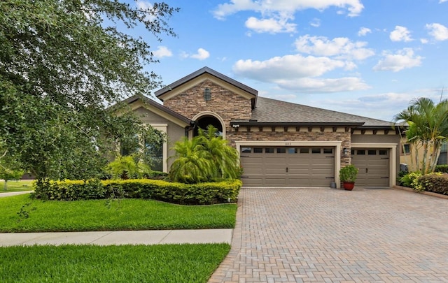 view of front of home featuring a garage, stone siding, decorative driveway, a front lawn, and stucco siding