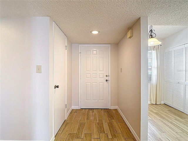 hall with light wood finished floors, a textured ceiling, baseboards, and recessed lighting