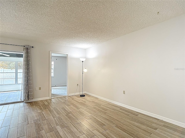 spare room featuring light wood-style floors, a textured ceiling, and baseboards