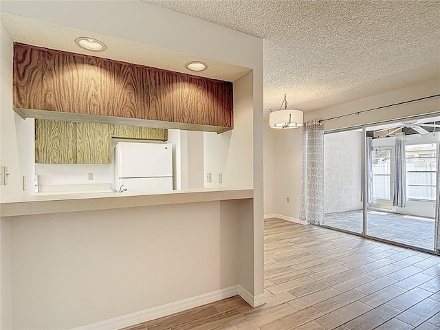 kitchen featuring freestanding refrigerator, wood finished floors, a textured ceiling, baseboards, and recessed lighting
