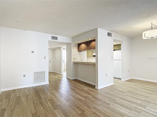 unfurnished living room featuring light wood-type flooring, a textured ceiling, and baseboards